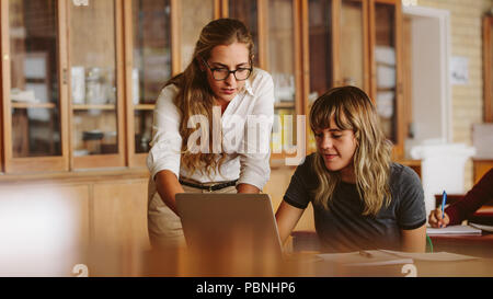 Female professor helping one of students at lecture. Teacher assisting the problem of a student in her classroom. Stock Photo