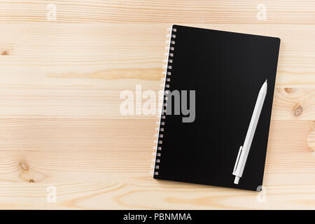 Design concept - Top view of black spiral notebook and wood pen on wood table background for mockup Stock Photo