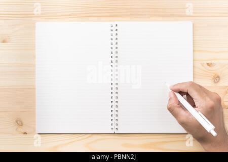 Design concept - Top view of black kraft spiral notebook and man's hand holding wood mechanical pencil on wood table background for mockup Stock Photo