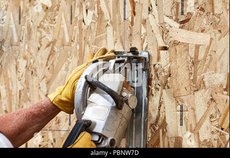 Carpenter cutting an opeing for a window on a new wall using a circular saw Stock Photo
