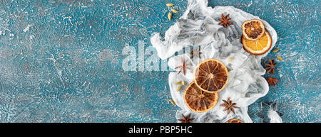 Dried orange slices, cinnamon sticks, anise stars, cardamom seeds in wooden bowls and metal biscuit molds on a blue background Stock Photo