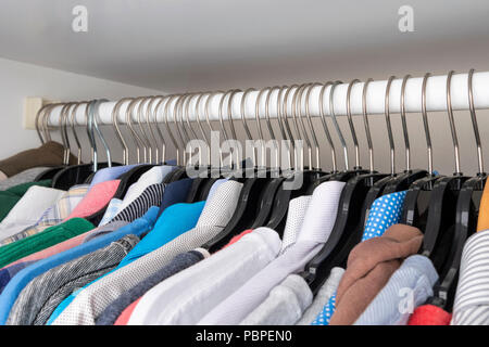 Choice of clothes of different colors hang on plastic hangers in a wardrobe Stock Photo