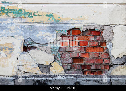 An old wall with peeling beige plaster under which red brickwork is visible. Stock Photo