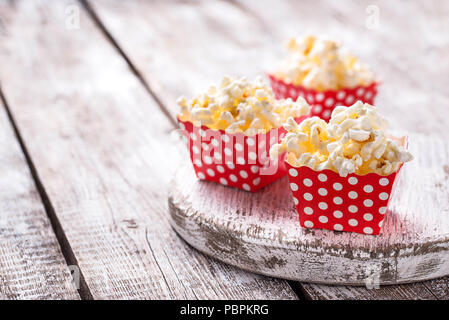 Popcorn in red polka dot pack on light wooden table. Selective focus