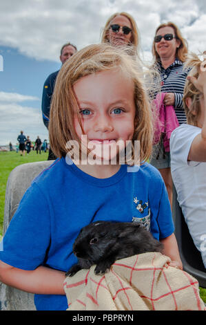 Schull, West Cork, Ireland. 29th July, 2018. Schull Agricultural Show is underway in blazing sunshine with hundreds of people attending. One of the many attractions is a pet farm - 6 year old Holly Quinn from Cork enjoyed petting a rabbit. Credit: Andy Gibson/Alamy Live News. Stock Photo