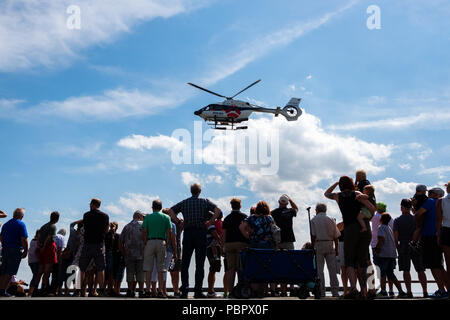 Wilhelmshaven, Germany. 29th July, 2018. Visitors watching a training mission of the rescue crew, in which a helicopter and the rescue cruiser Hannes Glogner are involved, during the Day of the German Society for the Rescue of Shipwrecked People (DGzRS) at the bay of Jadebusen. Credit: Mohssen Assanimoghaddam/dpa/Alamy Live News Stock Photo