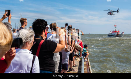 Wilhelmshaven, Germany. 29th July, 2018. Visitors watching a training mission of the rescue crew, in which a helicopter and the rescue cruiser Hannes Glogner are involved, during the Day of the German Society for the Rescue of Shipwrecked People (DGzRS) at the bay of Jadebusen. Credit: Mohssen Assanimoghaddam/dpa/Alamy Live News Stock Photo