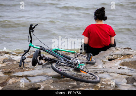 Wilhelmshaven, Germany. 29th July, 2018. A woman sits with headphones on the southern beach at the North Sea. Credit: Mohssen Assanimoghaddam/dpa/Alamy Live News Stock Photo