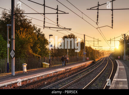 Waiting on a railway platform for a train in the early morning as the sun comes up. Bellshill Station, Glasgow, Scotland. Stock Photo