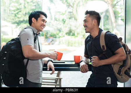 Side view of two cheerful young men talking and drinking coffee  Stock Photo