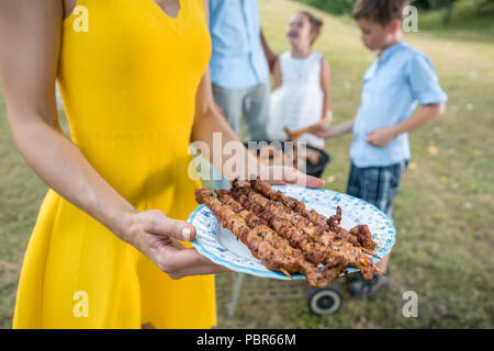 Close-up of hands of woman holding a plate with grilled steak skewers Stock Photo