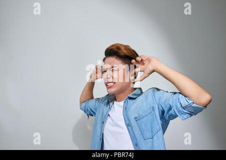 displeased man plugging ears with fingers doesn't want to listen isolated on gray wall background Stock Photo