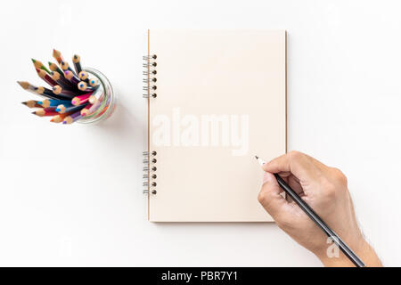 Design concept - Top view of kraft spiral notebook, blank page, pen holder and man's hand holding color pen isolated on white background for mockup Stock Photo