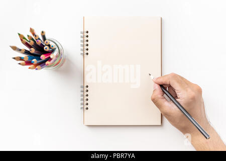 Design concept - Top view of kraft spiral notebook, blank page, pen holder and man's hand holding color pen isolated on white background for mockup Stock Photo