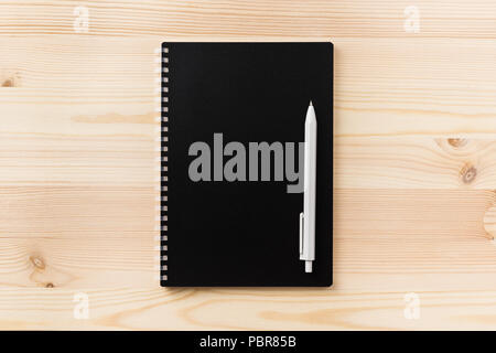 Design concept - Top view of black spiral notebook and wood pen on wood table background for mockup Stock Photo