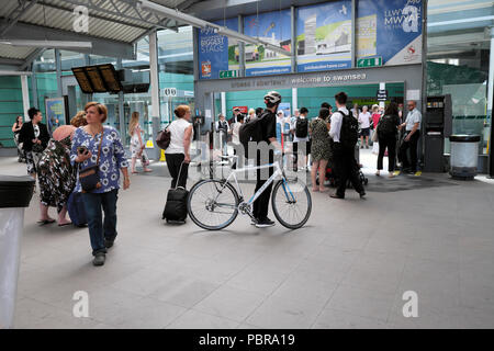 Cyclist with bike and passengers going through the ticket barrier after getting off a Great Western train from London in Swansea railway station Wales Stock Photo