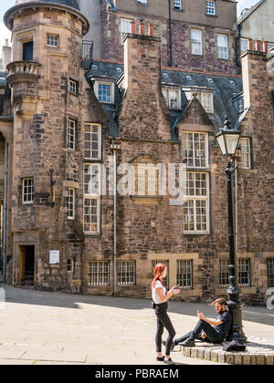 Young couple by old fashioned lamp post relax looking at phones and smoking in Makar’s Court outside Writer's Museum, Edinburgh, Scotland, UK Stock Photo