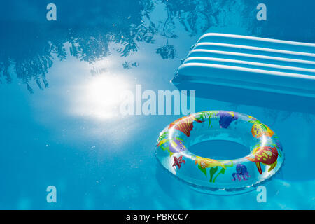 Inflated buoy and mattress floating on water of a swimming pool. Summer and holidays concept with ciopy space. Stock Photo