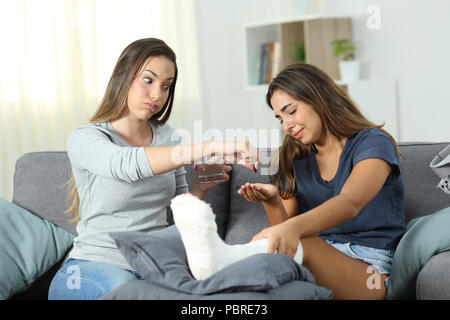 Disabled girl complaining and angry friend helping her sitting on a couch in the living room at home Stock Photo