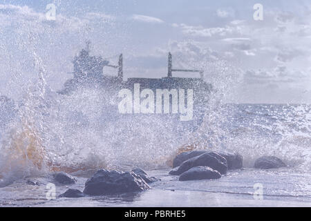 Silhouette of a commercial ship in a stormy Baltic sea through the spray of the waves on the rocks on the shore Stock Photo