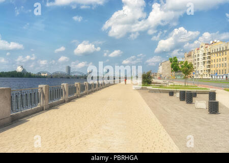 Cyclists ride on the Sunny quay on the Daugava river in Riga in the summer on the background of the bridges Stock Photo