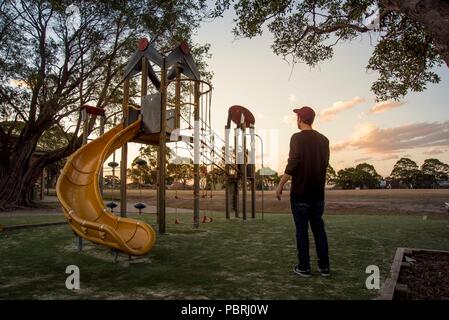 Caucasian boy looking at a yellow slide in a kids park during sunset. Stock Photo