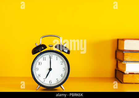 Alarm clock and book on yellow background with copy space. Stock Photo