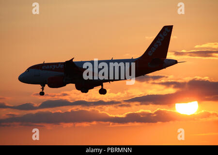 easyJet airbus A319 plane G-EZDE is silhouetted as it passes in front of the setting sun whilst making its way in to land at Edinburgh airport Stock Photo
