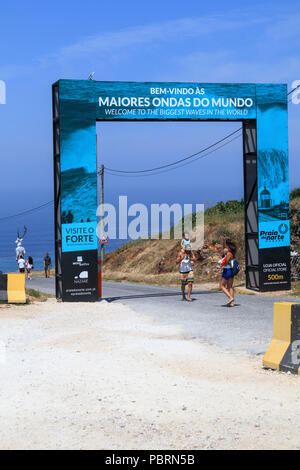 Tourists beneath the large 'Welcome to the biggest waves in the world' entrance gateway at Nazare Portugal Stock Photo