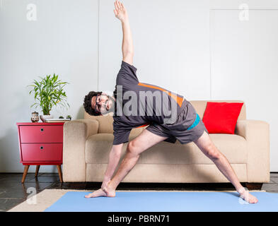 Beautiful caucasian bearded man in black clothes on blue yogamat doing triangle pose Stock Photo