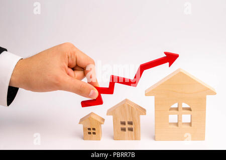 businessman's hand holds the red arrow up above the houses. The concept of growth in demand for real estate. Increase in the value of property, capita Stock Photo