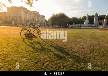 A lady snoozes by her bike outside Buckingham Palace on parched grass of a hot summer Stock Photo