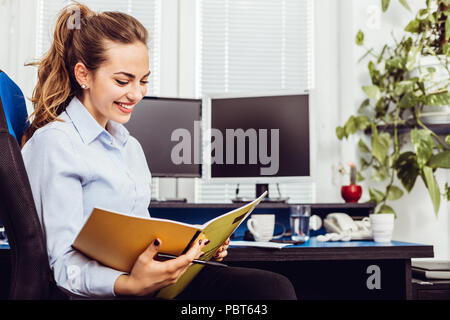 Business and people concept - smiling woman holding papers/ files and drinking coffee in office Stock Photo