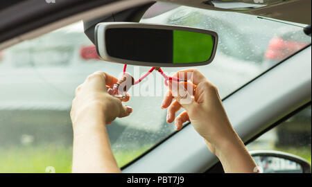 A woman's hand knots an air freshener on a mirror, close-up Stock Photo