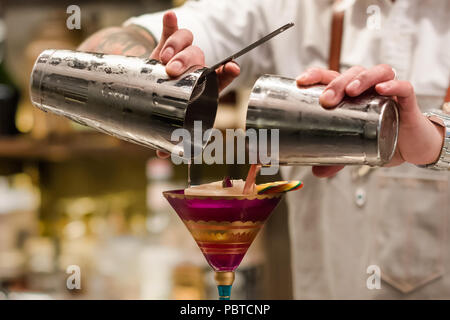 Professional bartender pouring cocktail from the shaker into the glass. Barman holding in hands cocktail tool. Mixing alcoholic drink process. Stock Photo