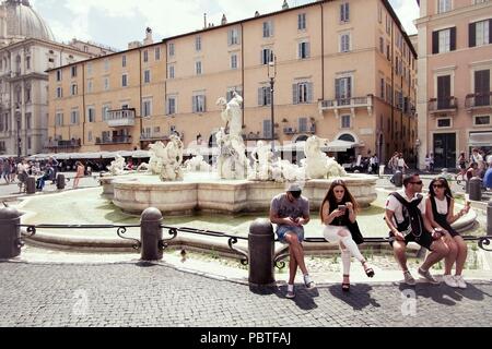 ROME, ITALY - 29 JUNE 2018: Tourists rest in the famous Piazza Navona, Rome, Italy, with a fountain with statues behind it Stock Photo