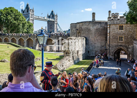 Beefeater giving Tower of London tour in shadow of Tower Bridge, taken in London, UK on 8 July 2017 Stock Photo