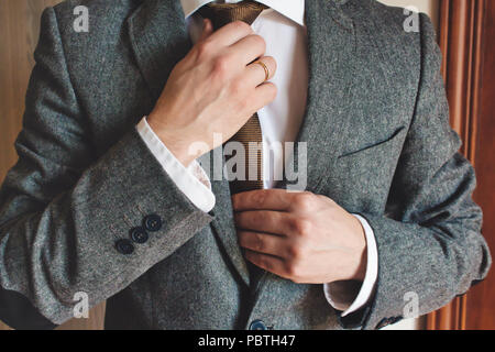 Man in smart suit wearing wedding ring adjusting tie Stock Photo