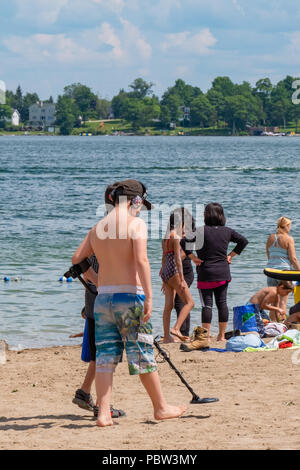 Young boy searches Couchiching Beach in Orillia Ontario with a metal detector looking for coins and other precious metals. Stock Photo