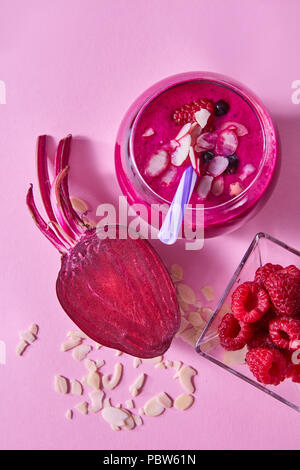 Healthy breakfast red smoothies from berries in a glass with half of beet with nuts flakes in a glass on a pink paper background. Stock Photo