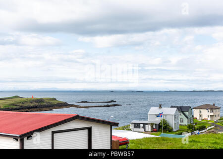 Stykkisholmur, Iceland national country flag with blue, red stripes in wind on cloudy overcast day, cityscape skyline of small fishing village town on