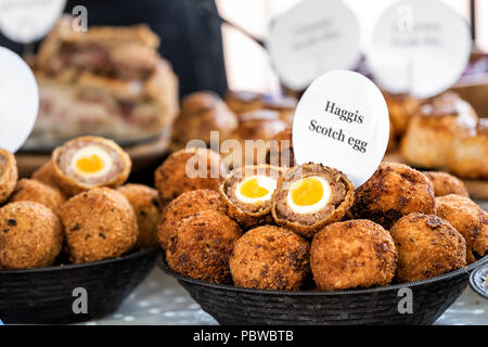 Closeup bowl of Haggis Scotch deep fried eggs with sign in market street food fair, cross section cut open, yellow yolk, breading tradition English fo