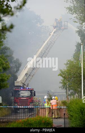 Glasgow, UK. 30th July, 2018. Glasgow, Scotland, UK. A large fire forces the closure of Crookston Rd in Glasgow as fire appliances line the street and firefighters use breathing apparatus and high reach platforms to tackle the blaze. Stock Photo