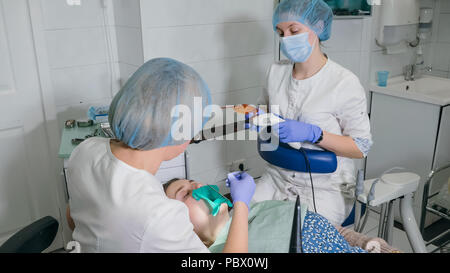 Woman at dentist clinic gets dental treatment to fill a cavity in a tooth. Dental restoration and composite material polymerization with UV light and laser. Stock Photo