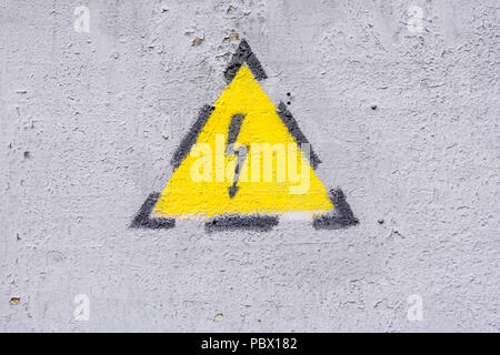 Danger of electrocution yellow sign on gray painted wall. High voltage warning sign. Electric bolt in yellow triangle safety symbol: caution, risk of  Stock Photo