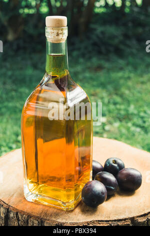 Plum brandy (slivovitz) in glass bottle with fresh ripe plums on a wooden surface. Stock Photo