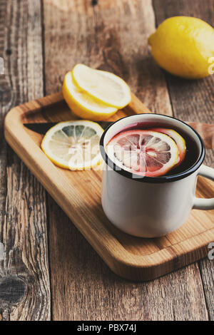Hot fruit tea with lemon slices in white rustic mug on wooden table, cozy hot winter drink Stock Photo