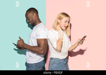 Mixed raced couple of students taking mobile phones. Caucasian girl and her African boyfriend posing at studio . Stock Photo