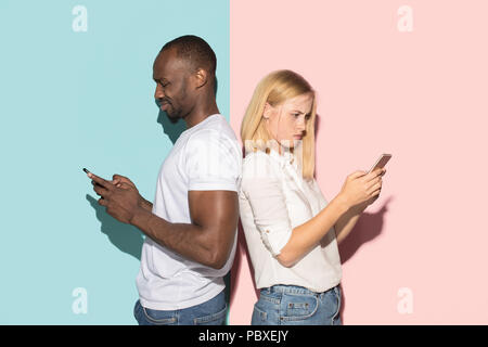 Mixed raced couple of students taking mobile phones. Caucasian girl and her African boyfriend posing at studio . Stock Photo