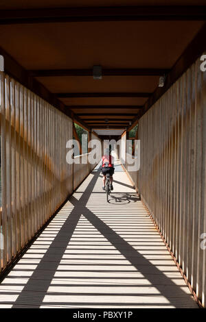 A female cyclist crossing a covered wooden bridge in Norway Stock Photo